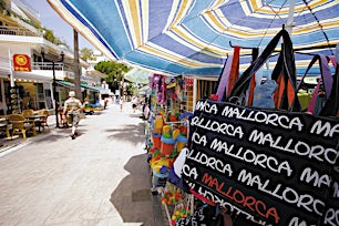 Kävelykatu jonka yllä riippuu värikkäitä varjoja ja myynnissä lukee Mallorca