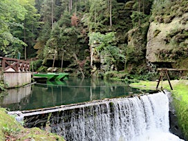 Vehreä metsämaisema, jossa on pieni pato ja virtaava joki.
