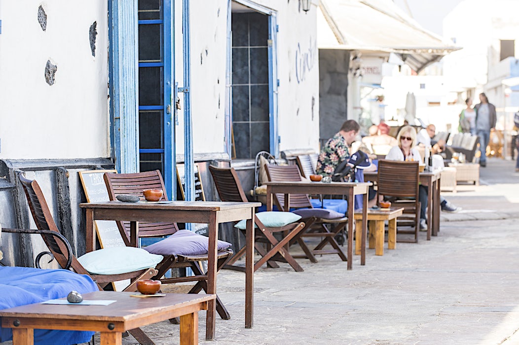 Ravintola kadun varrella, puisia tuoleja ja valkoisia seiniä