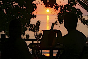 Kaksi ihmistä istuu terassilla katsellen auringonlaskua meren yllä.