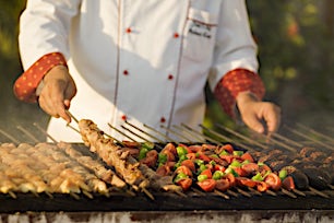 Kokki grillaa värikkäitä kasviksia ja lihavartaita ulkokeittiössä.