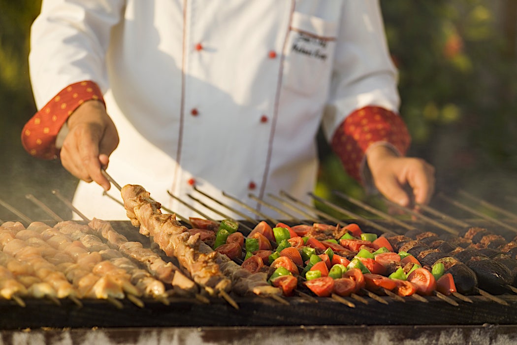 Kokki grillaa värikkäitä kasviksia ja lihavartaita ulkokeittiössä.