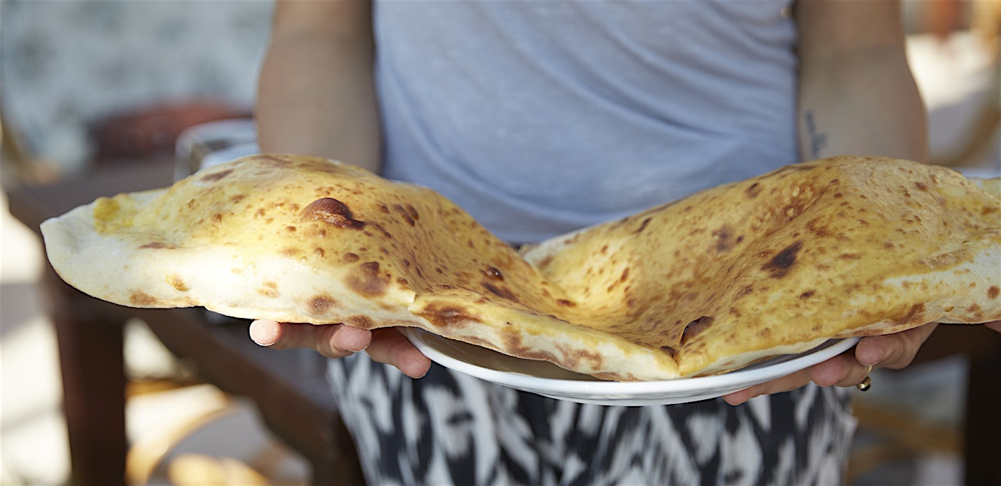 Henkilö pitelee kädessään lautasta, jolla valtava, rapea leipä.
