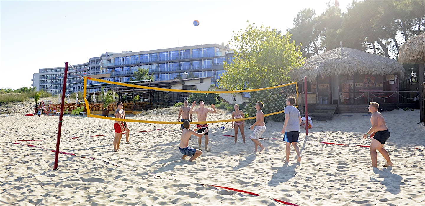 Ihmiset pelaavat rantapelivolleyta hiekalla, taustalla rakennuksia ja puita.