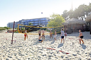 Ihmiset pelaavat rantapelivolleyta hiekalla, taustalla rakennuksia ja puita.