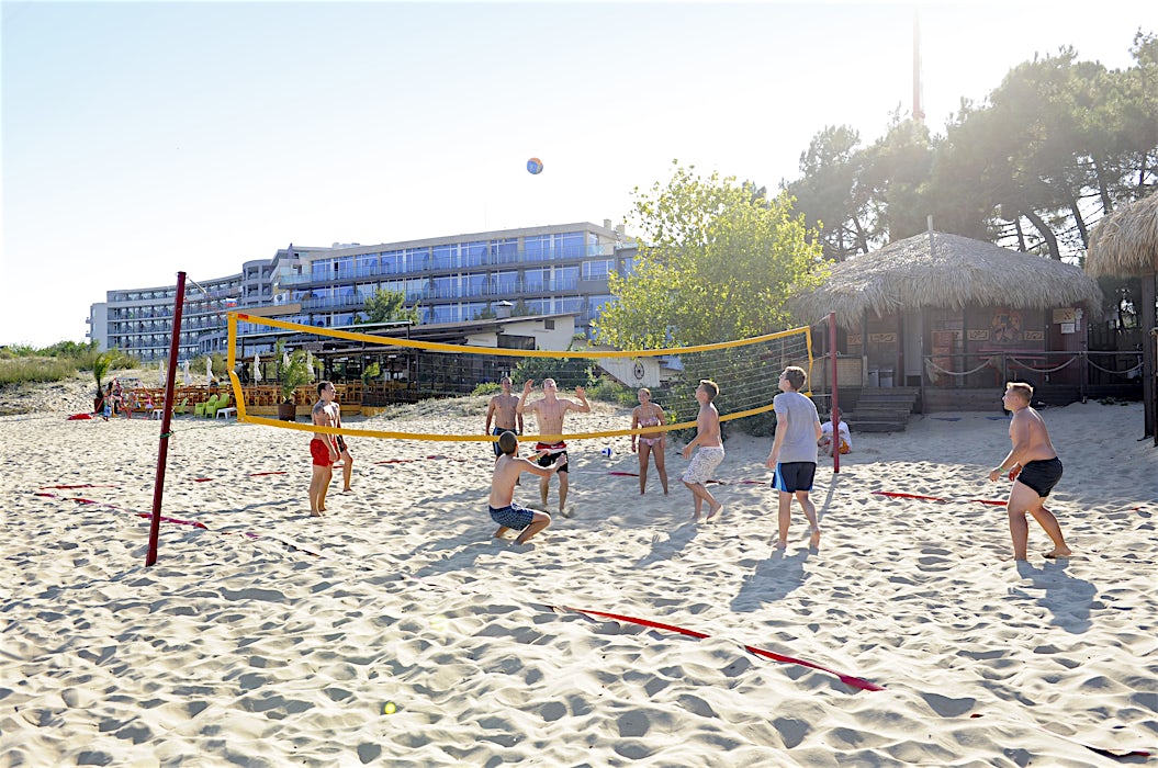 Ihmiset pelaavat rantapelivolleyta hiekalla, taustalla rakennuksia ja puita.