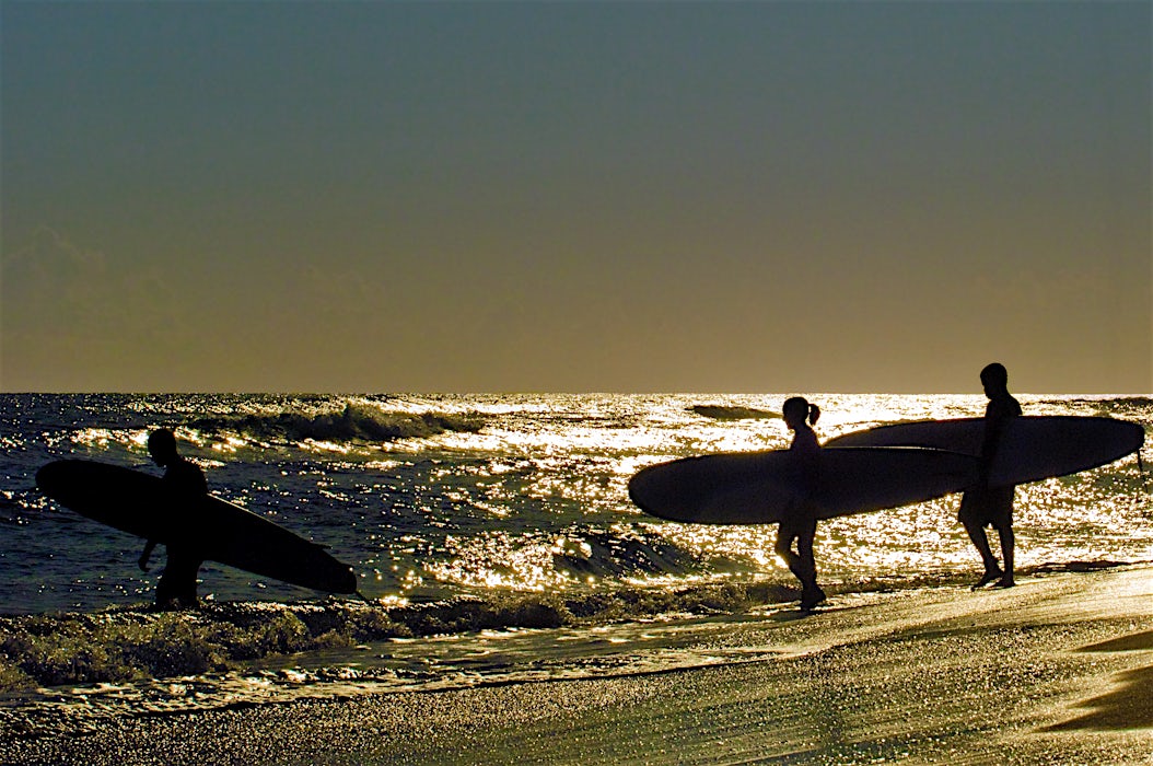 surffaajia kantamassa lautojaan auringonlaskussa kimaltelevassa meressä