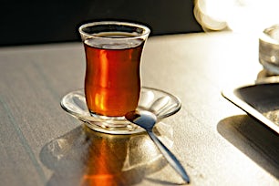 Lasi turkkilaista teetä lautasella ja lusikka vieressä pöydällä.