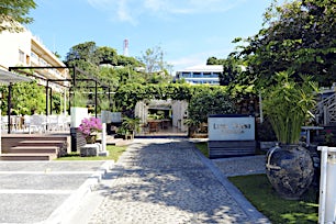 Rauhallinen piha-alue, jolla terassi vasemmalla ja keskellä kivetty polku vehreään pergolaan.