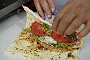 Kädet valmistamassa täytettyä leipää tai wrapia tuoreista vihanneksista.