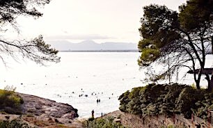 Kallioinen rantapoukama ja uimareita kuvattuna ylhäältä.