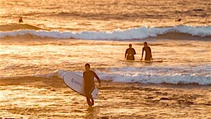 surffaajia rannalla ilta-auringon kultaisessa valossa
