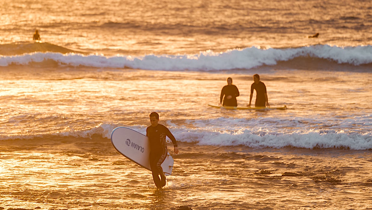 surffaajia rannalla ilta-auringon kultaisessa valossa